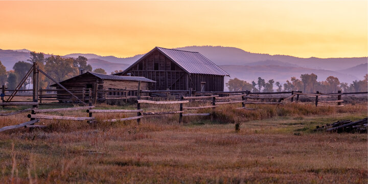 Mormon Row in Grand Teton National Park. A large, old barn sits in a field with a beautiful sunset in the background