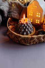 Winter still life. Tray with season decor burning candle shape of tree, ceramic houses and cozy gray sweater. Christmas cozy winter home decor. Copy space