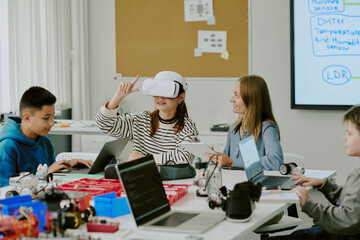Teacher with smile looking at girl who enjoying VR game and trying to describe it while...