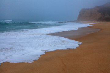 Waves gently wash onto a quiet sandy shore, creating soft, foamy