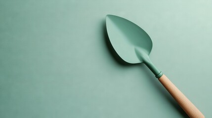  A green spatula with a wooden handle on a light green background features a wooden handle at its tip