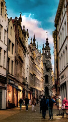 Naklejka premium A vibrant street scene in the heart of Brussels as evening falls. The beautiful historic architecture lines the street, leading to the striking view of the famous city tower under a colorful sky.