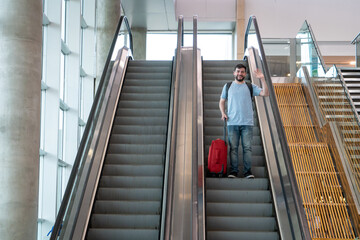 Viajero saludando desde las escaleras mecánicas de un aeropuerto