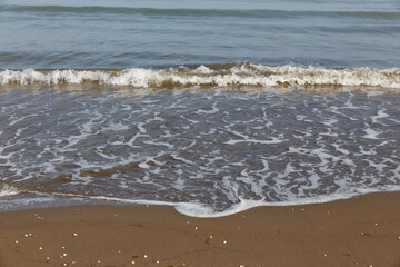 Beach with waves and white foam on the sand and sea background. Caspian Sea