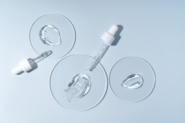 Two pipettes with gel smears on a laboratory circle glass on blue background, sterile cosmetics concept
