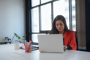 Latin Woman working in coworking is typing on laptop