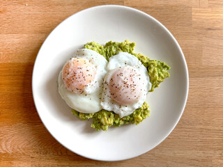 Two poached eggs on smashed avocado on a small round white plate