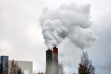 Industrial Emissions. A factory building with a prominent chimney releasing steam into the sky. The balance between industrial production and environmental impact, growth and sustainability.