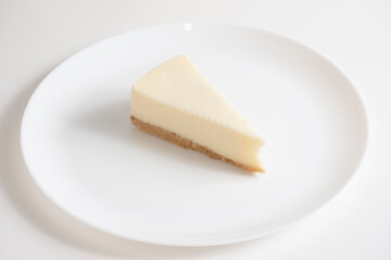 Traditional cheesecake on a white plate on a white background.