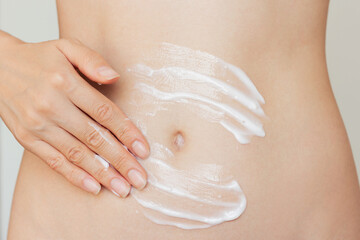 Close up young woman applying a white moisturizing and nourishing cream to the skin of her slim...