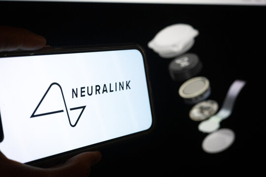 Silhouette of Hand Holding Phone with Neuralink Logo in Front of Neural Interface Technology Website on Computer Screen