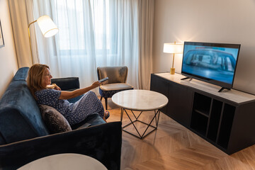 Elderly lady watches TV on the sofa in the living room at home