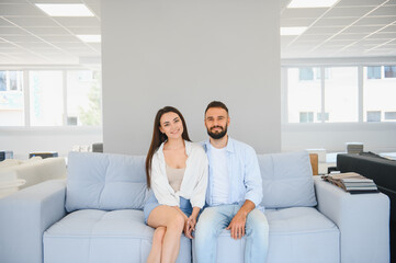 Couple of young man and woman shoppers choose comfortable sofa in department of furniture store