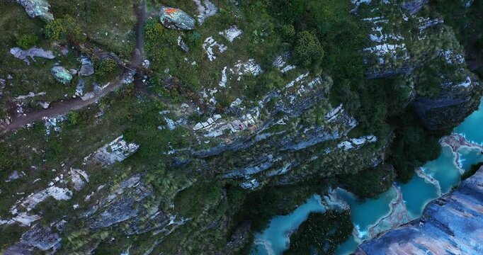 Amazing overhead drone shot of a person artist in brightly colored costumes dancing down the mountains around the purple water Millpu lake.
