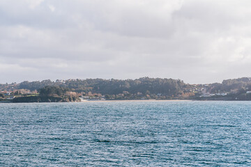 Fototapeta premium A peaceful coastal landscape featuring the ocean and the lush, forested shoreline of A Coruna, Spain