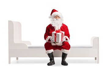 Santa Claus holding a present box and sitting on a bed