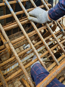 Lightning conductor connection to foundation rebar for grounding and surge protection. Worker securing ground connection on reinforced concrete foundation.