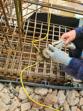 Lightning conductor connection to foundation rebar for grounding and surge protection. Worker securing ground connection on reinforced concrete foundation.