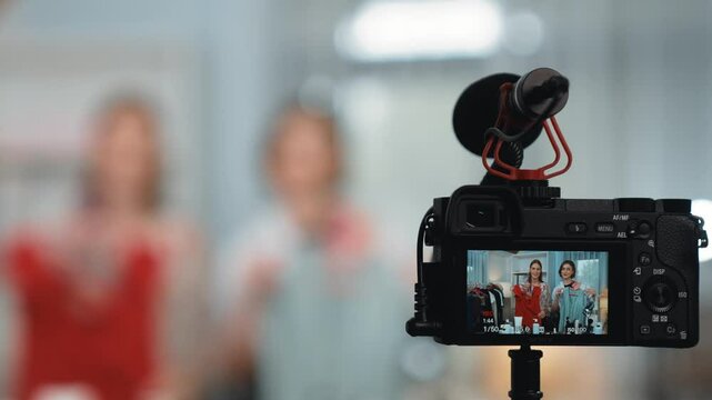 Rear view behide camera screen display two women influencer shoot vlog video review clothes prim social media or blog. Girls with apparel studio lighting for live streaming marketing recording session