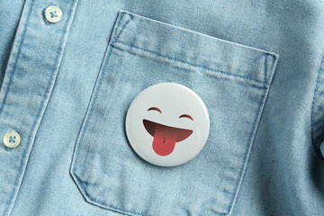 Badge with face showing tongue attached to pocket of denim shirt