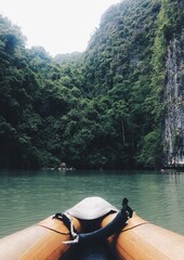 The orange bow of an inflatable canoe, on the smooth water surface of the bay, in front of the bow of the canoe lies an island with steep cliffs and green jungle.