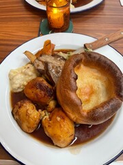 Traditional British Sunday Roast Dinner with Yorkshire Pudding, Roast Potatoes, Lamb, and Gravy – Cozy Candlelit Pub Meal