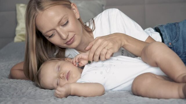Happy mom hugging and touching sleeping newborn baby. Cute newborn baby sleeping in bed at home. Family care, happy childhood and motherhood, close up