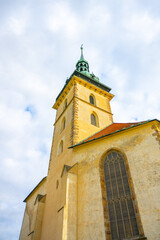 Fototapeta premium The Church of the Assumption of the Virgin Mary in Most showcases stunning late Gothic architecture against a backdrop of a cloudy sky, highlighting its impressive spire and detailed facade.