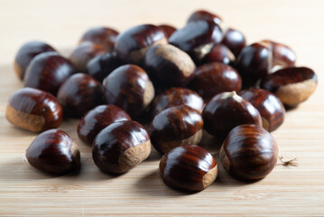 Close-up of autumn raw shiny chestnuts in a pile on a wooden table