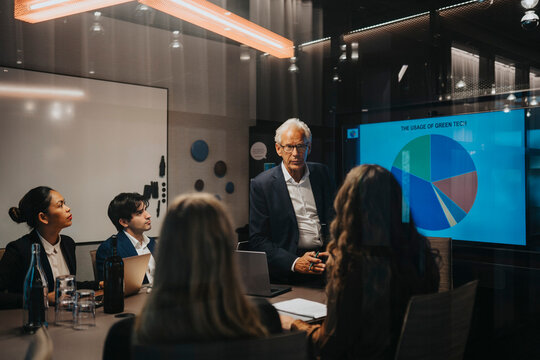 Senior businessman discussing plans with male and female colleagues in board room