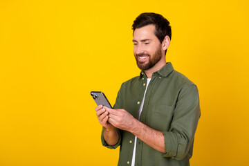 Portrait of nice young man use phone empty space wear khaki shirt isolated on yellow color background