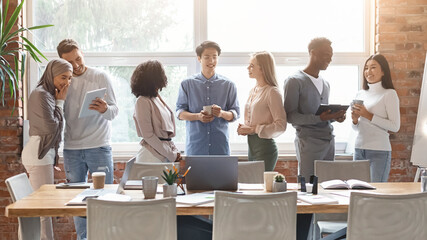 Group of multiethnic young people having friendly conversation while coffe break at business...