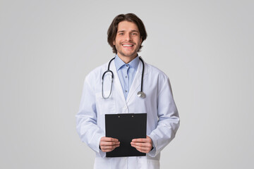 Portrait Of Smiling Male Therapist Posing With Clipboard In Hands Over Light Studio Background, Copy Space