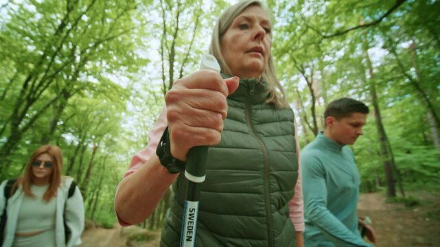 People walking use Scandinavian trekking sticks and hold nordic poles in green forest. Group