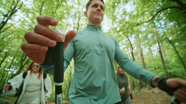 Group of people walking use Scandinavian trekking sticks. People hold nordic poles in green forest