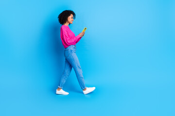 Full body photo of attractive young woman walk hold device dressed stylish pink clothes isolated on blue color background