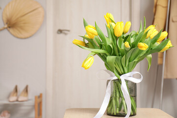 Vase of yellow tulips with white ribbon in hallway