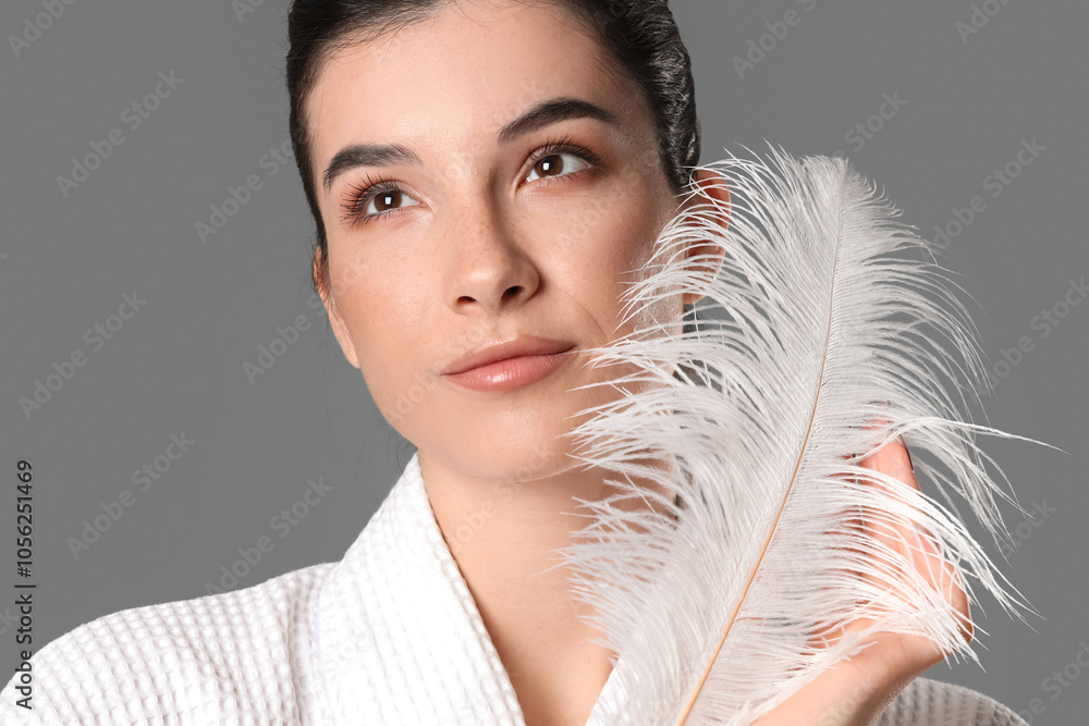 Wall mural beautiful young woman with soft feather on grey background. depilation concept