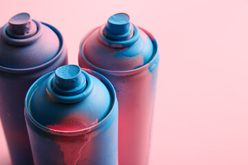Spray paint cans on pink background, closeup