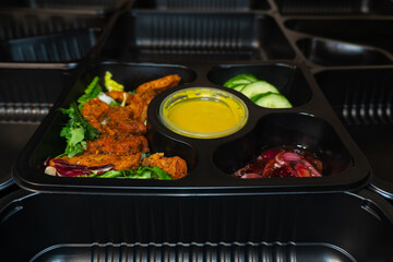 A recyclable black container with salad ingredients against a background of black containers. This choice highlights an eco-friendly approach to healthy eating and meal delivery.