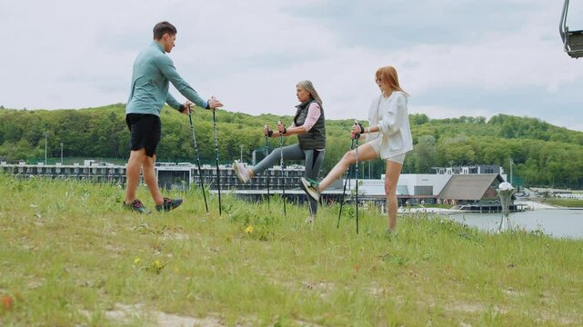 Outdoors trainer shows how to use Scandinavian trekking sticks. People hold nordic poles in green forest park with lake