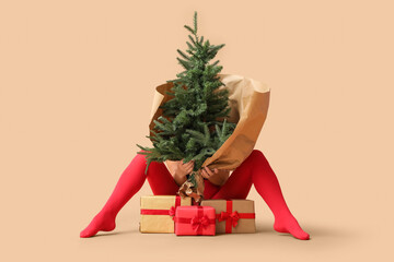 Legs of beautiful young sexy woman and Christmas tree with gift boxes on beige background