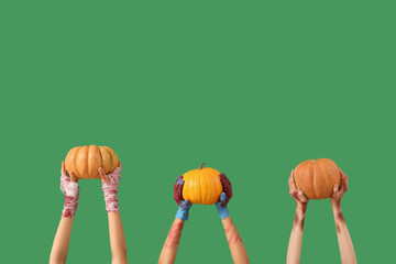 Hands of zombies with ripe pumpkins on green background. Halloween celebration