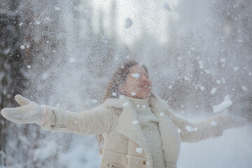 A woman dressed in a pristine white coat is joyfully throwing snow into the air, creating a beautiful scene all around her