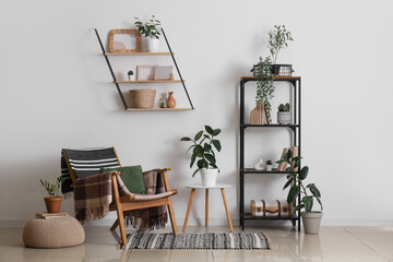 Interior of stylish modern room with armchair, houseplants and shelving unit near white wall