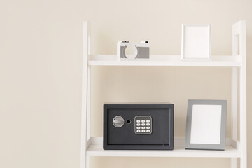 Shelving unit with blank frames and safe box near beige wall at home