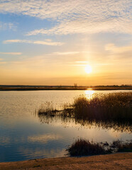 Obraz premium A peaceful sunset over a calm lake, with golden hues and soft clouds reflected on the water.
