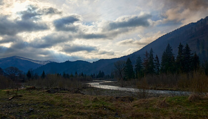 A winding river flows through a tranquil valley surrounded by forested mountains under an overcast sky