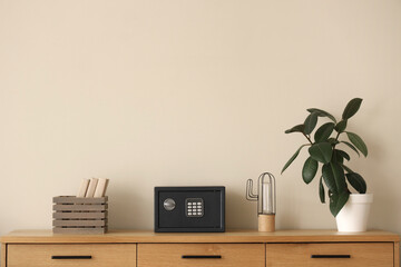 Safe box with books and houseplant on commode near beige wall