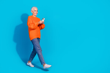 Photo of old lady walking using blogging gadget wear denim clothes isolated blue color background